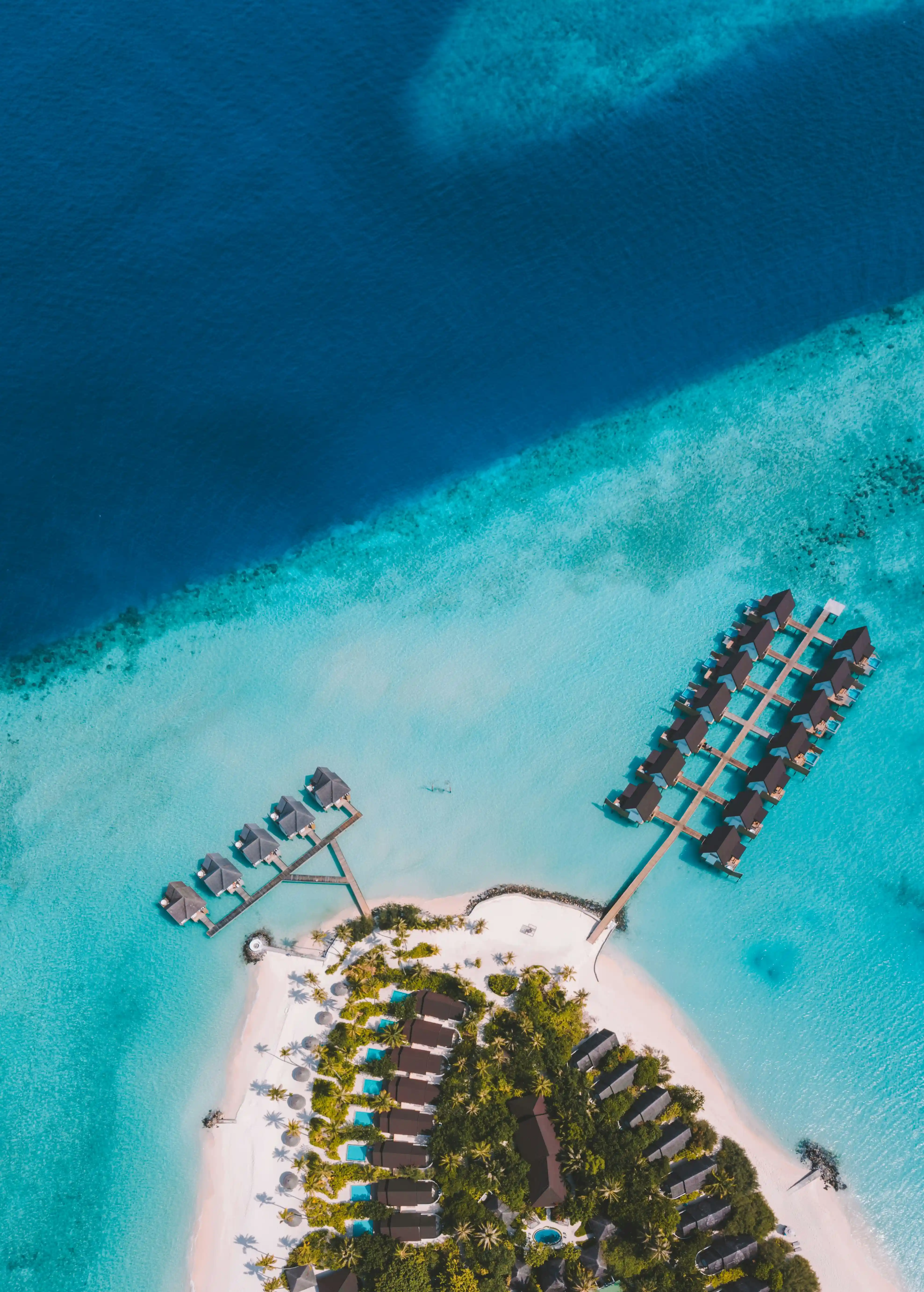 A resort island in the Maldives with two water villa jetties, seen from above